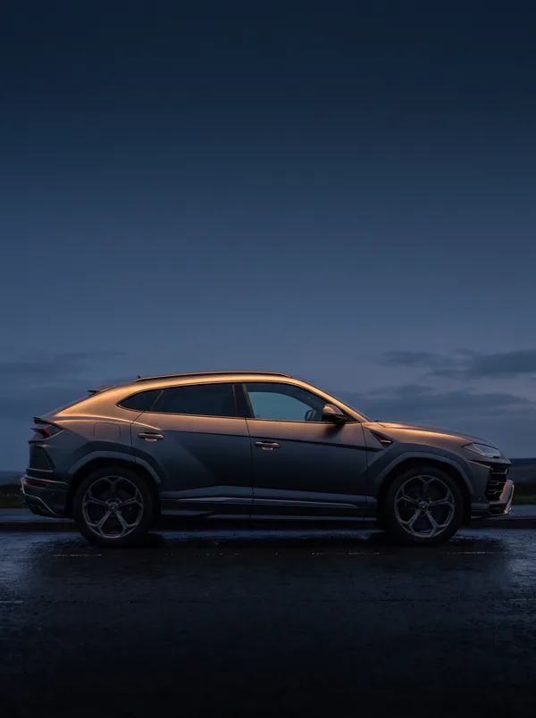 Grey Lamborghini Urus side-on at dusk on a wet road