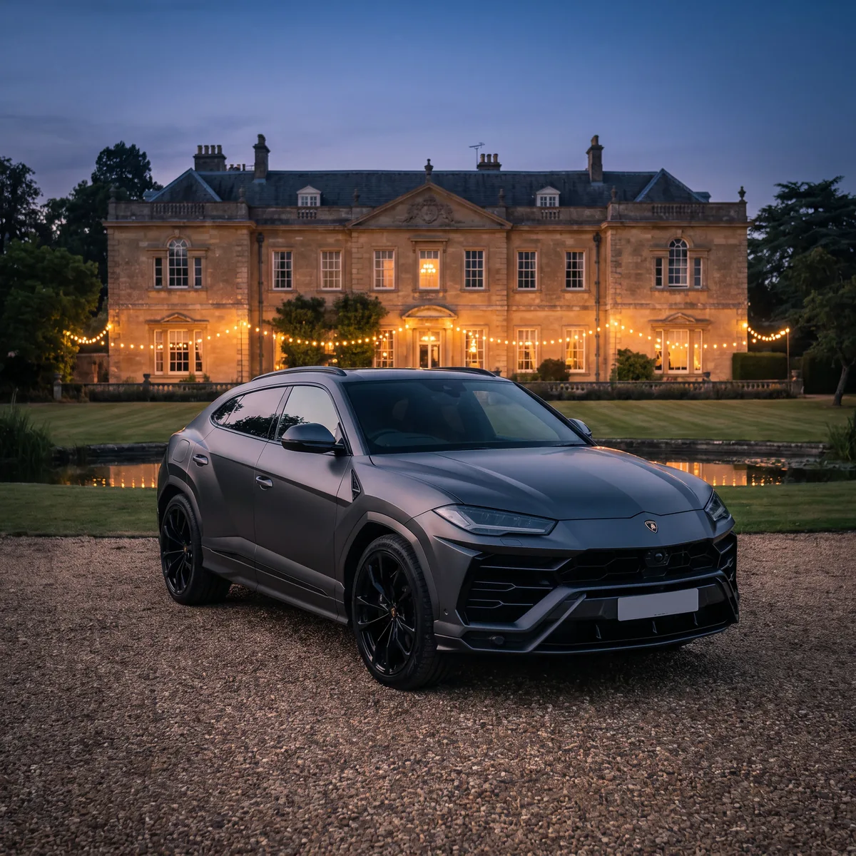 Grey Lamborghini Urus wedding car parked outside a lit country-house wedding venue at dusk