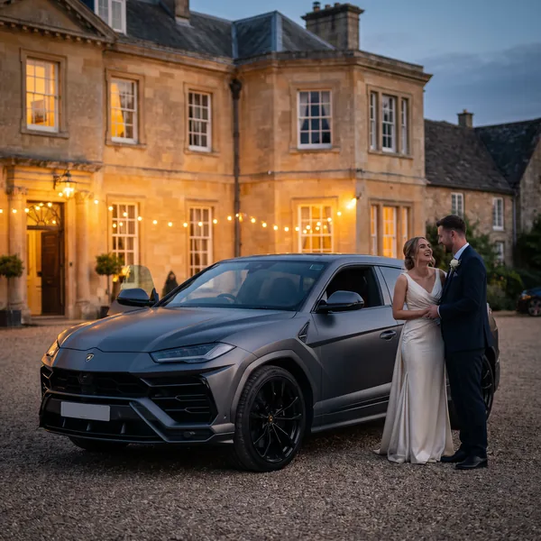 Bride and groom beside the chauffeur-driven Lamborghini Urus on a manor house forecourt at dusk